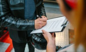 A biker man wearing leather jacket and holding helmet signing insurance policy 
