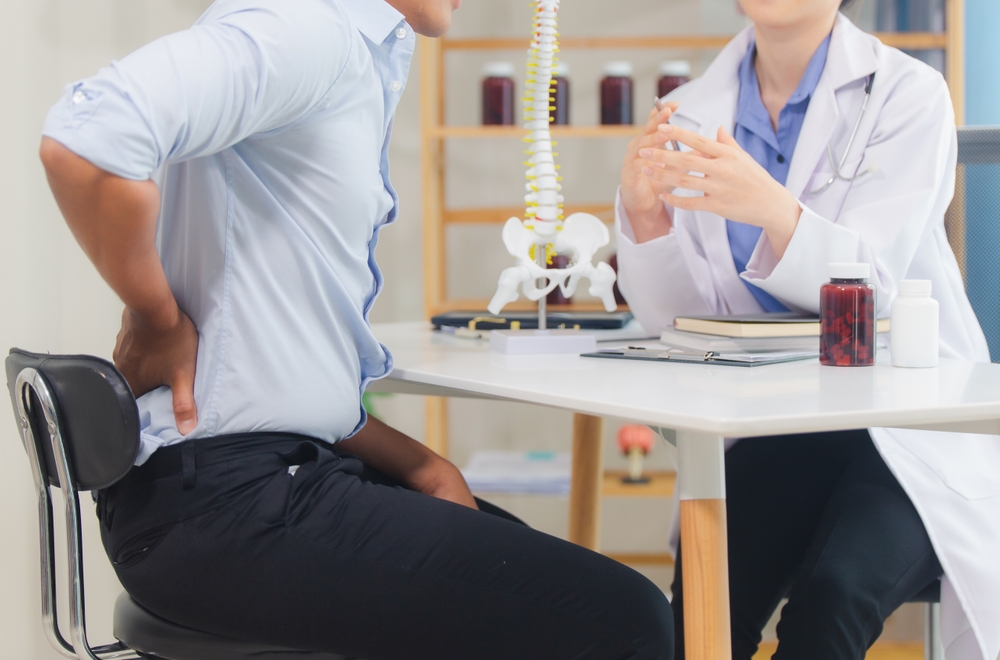 Patient experiencing lower back pain during a spinal cord injury consultation with a doctor