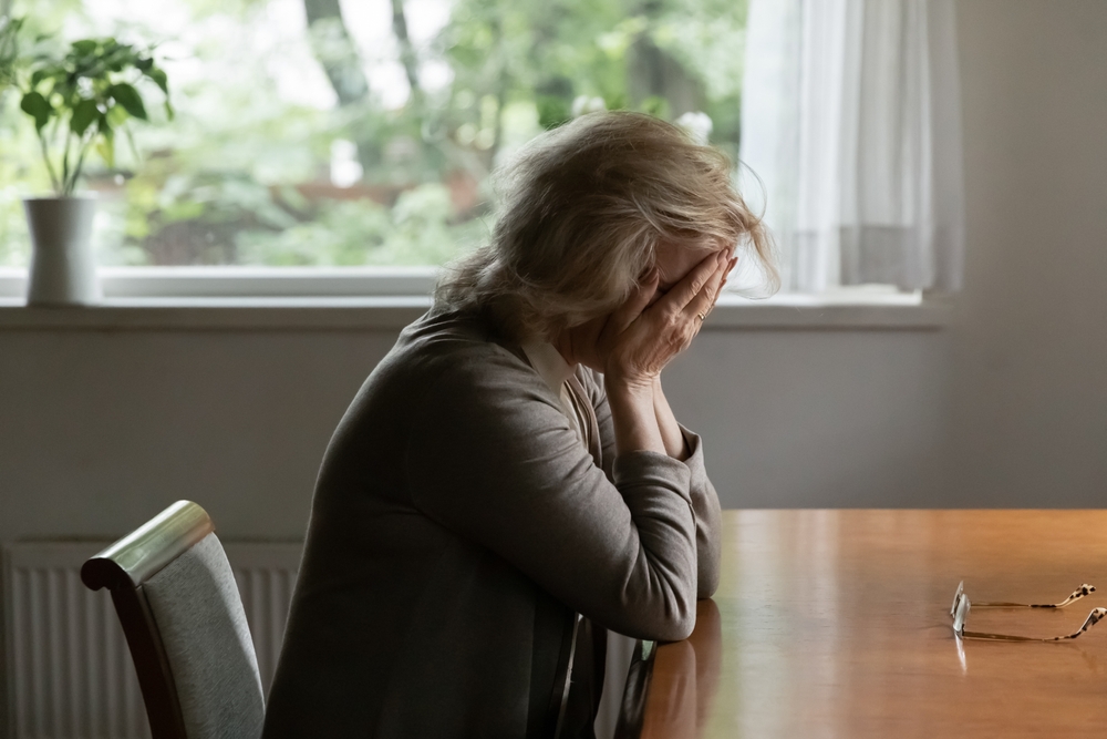 How To Claim Pain and Suffering From an Auto Crash 1 Older woman sitting at a table with her face in her hands, appearing overwhelmed after an accident-related injury