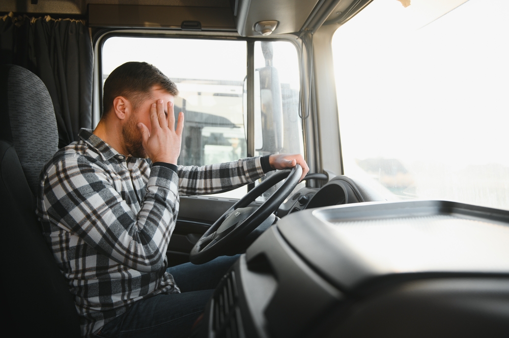 Fatigued truck driver holding his face while sitting behind the wheel.